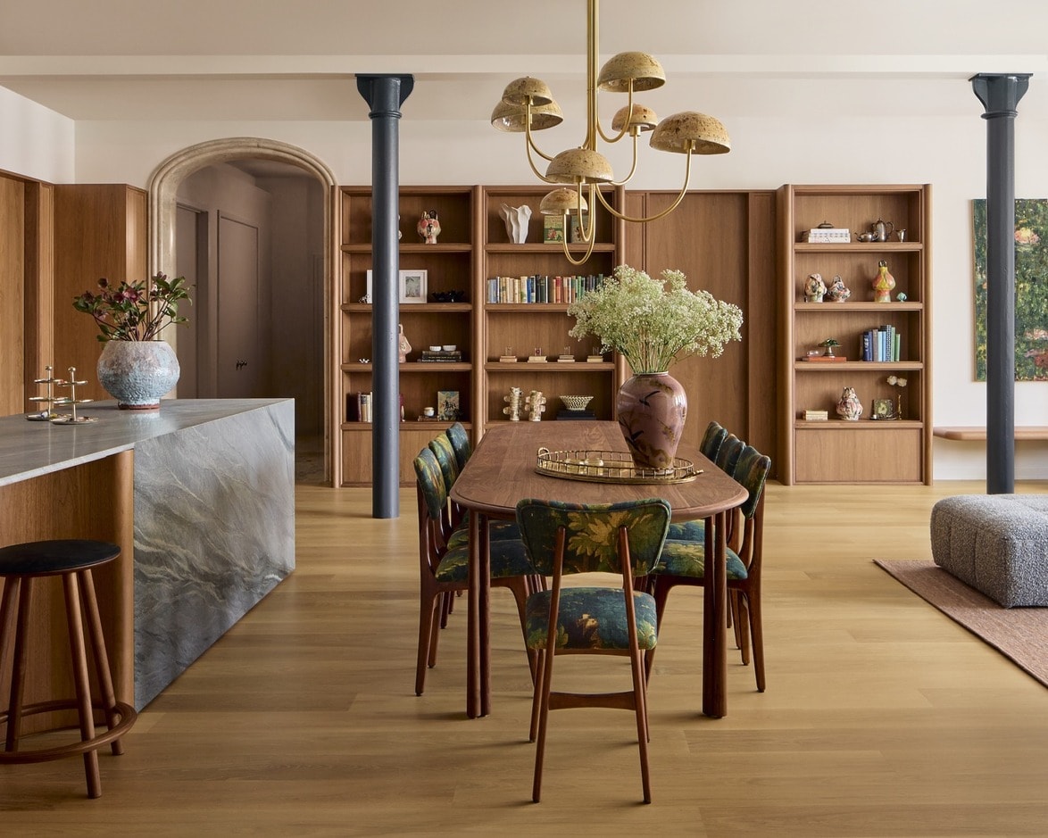 Modern dining room with wooden table, floral chairs, elegant chandelier, and built-in bookshelves in a spacious interior.