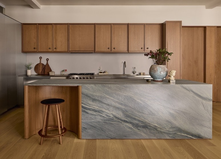 Modern kitchen with wooden cabinets, island with marble countertop, bar stool, and decorative vase with flowers.