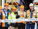 ribbon cutting with oversize scissors at a frozen food plant, with multiple people wearing personal protective gear and hard hats