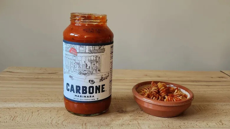 Carbone's jarred marinara sauce next to a small bowl prepared on top of a wooden table.
