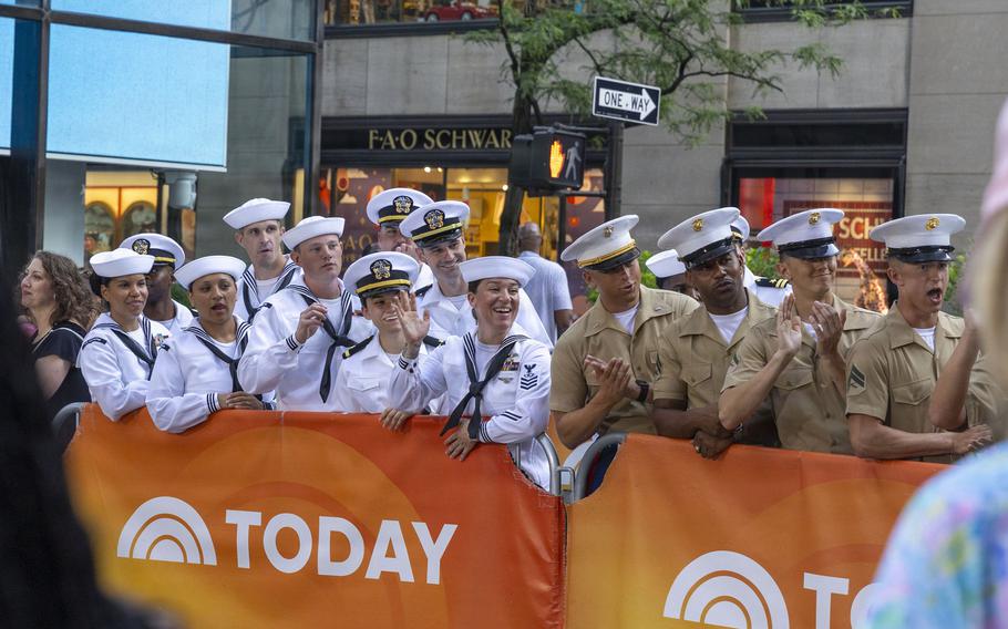 Sailors and Marines stand behind rails covered with banners that mark the Today show.