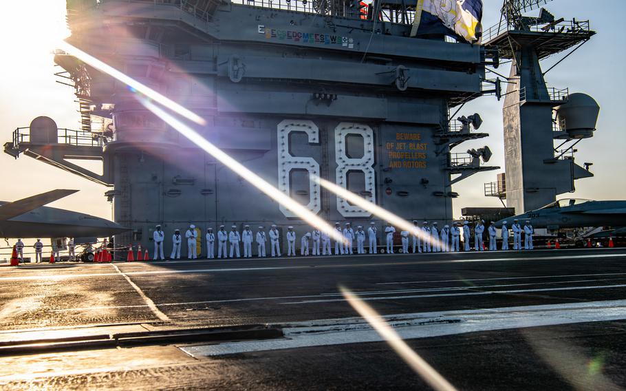 The sailors stand on the flight deck next to the island. No. 68, signifying Nimitz, is painted on the side.