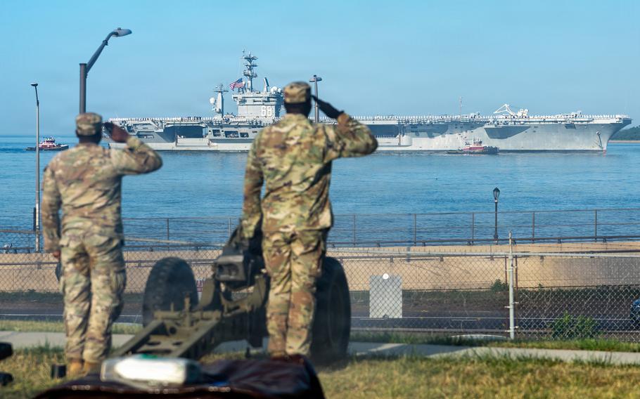 Two service members standing on land salute Nimitz as it cruises past.
