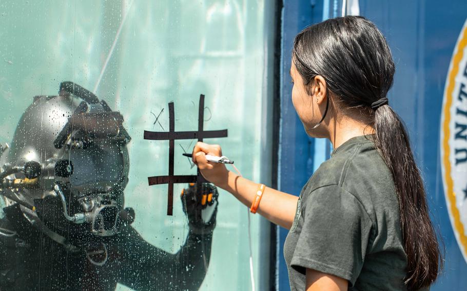 A young girl marks an X in the center square painted on the side of the tank withe diver inside.