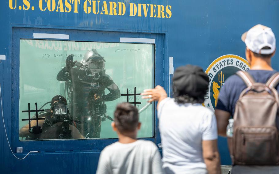 Two divers look out from inside the tank as people pass by.