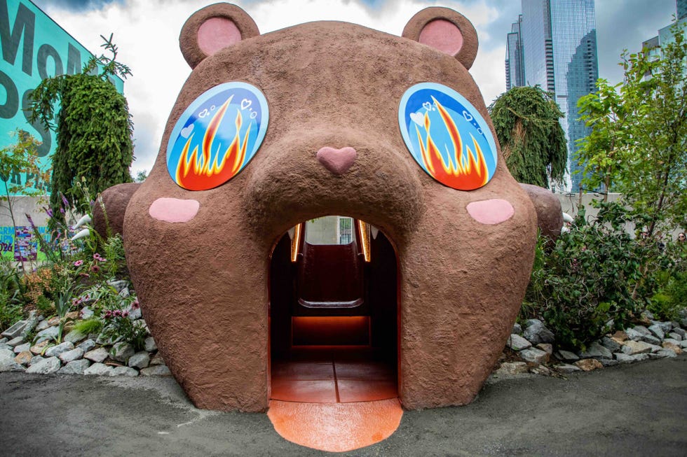 A whimsical bear-shaped structure with colorful fiery designs and a tunnel entrance, surrounded by greenery.