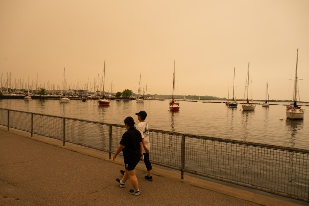 People walk on the waterfront in Toronto as wildfire smoke fills the city, on Wednesday, July 15, 2026. (Laura Proctor/The Canadian Press via AP)