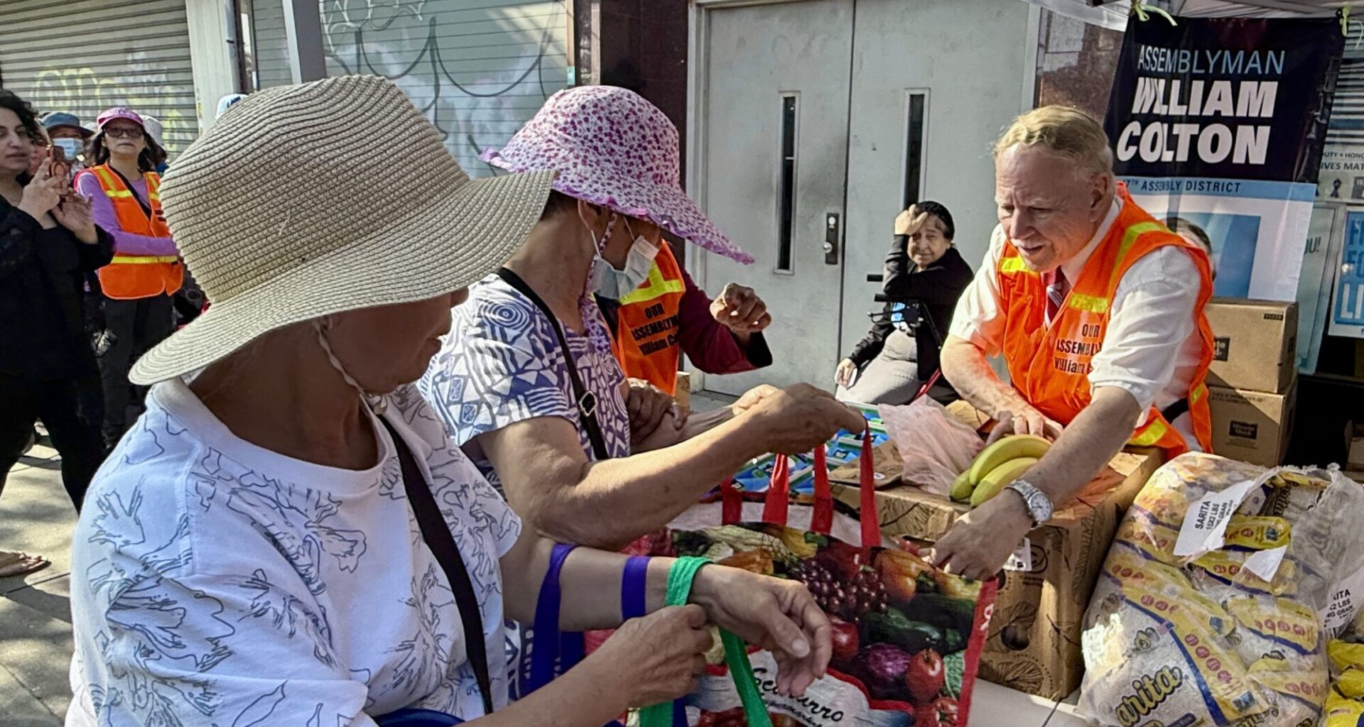 Assemblymember William Colton hands bunches of bananas to area residents at the free food distribution outside his office on Thursday, July 23. Photo: Office of Assemblymember William Colton