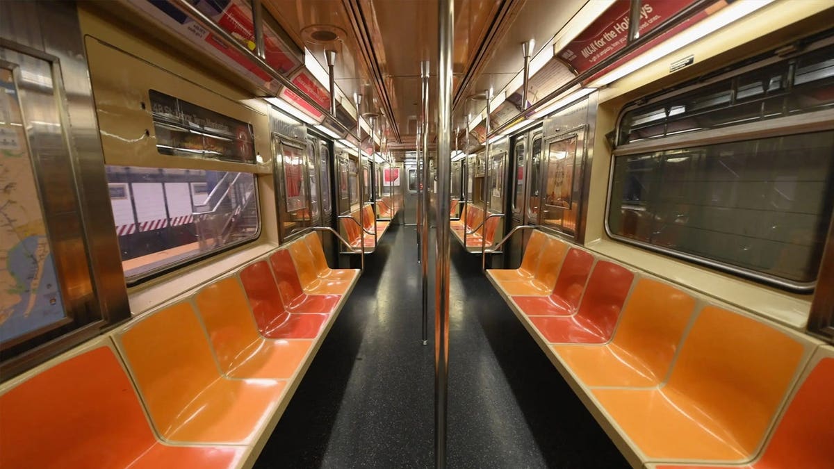 An empty New York subway car interior with rows of seats and handrails.