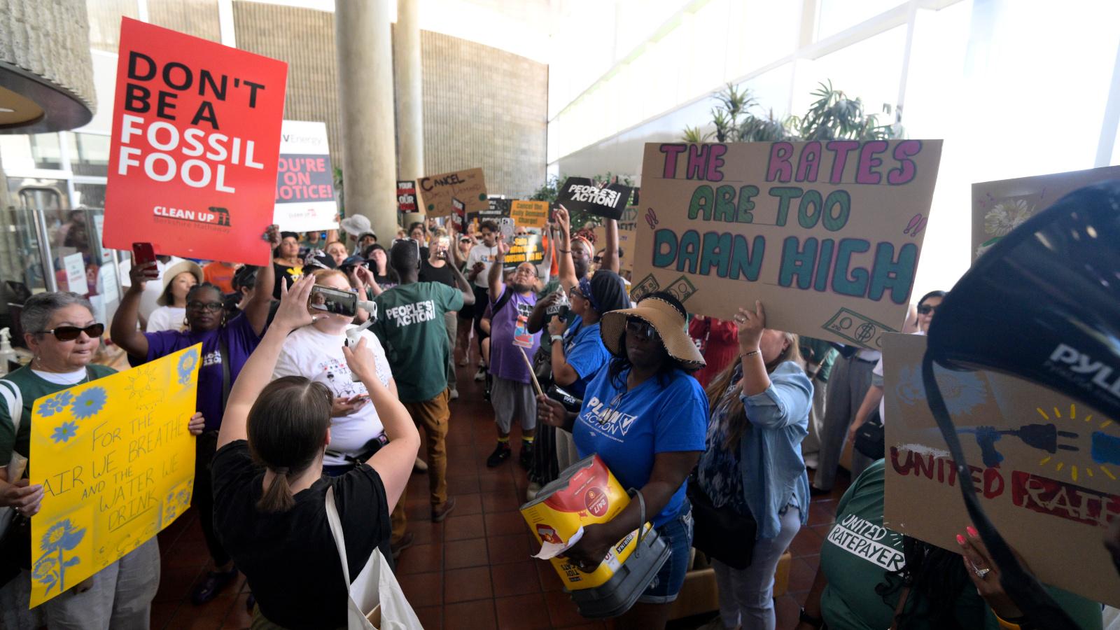 Photo of people protesting in a crowded hallway, with one sign reading "Don't be a fossil fool"