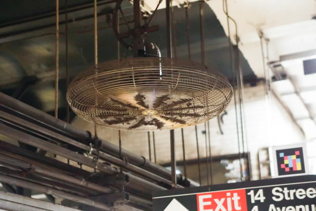 Subway fan is covered in dust at Union Square station. The exit sign for 14th street and 4th avenue can be seen out of focus in the lower third of the frame.