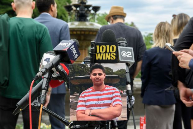 A photo of Romanch Mahajan hangs from the lectern among news microphones Monday, June 22, 2026, in Central Park. (Evan Simko-Bednarski / New York Daily News)