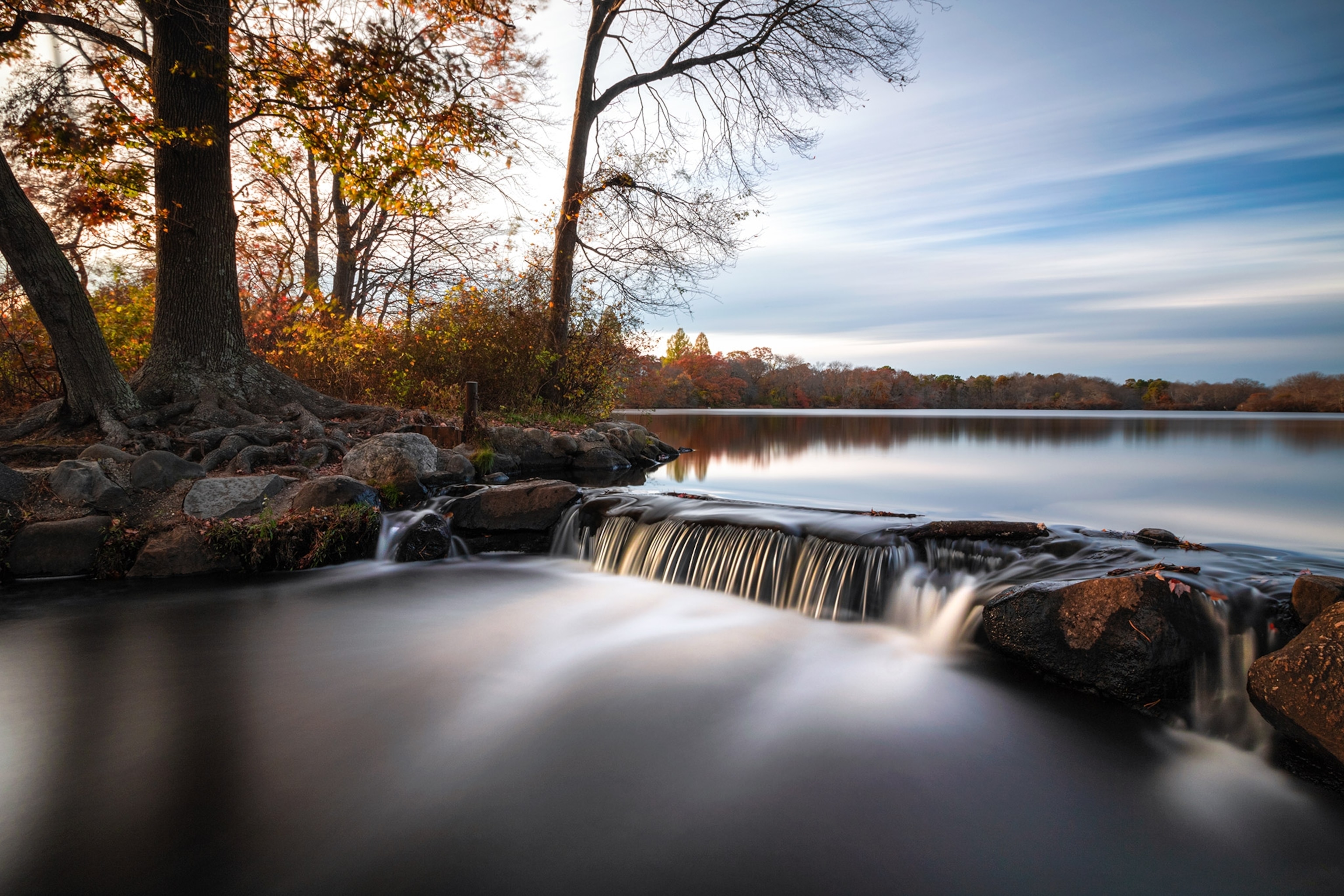 Long exposure photograph showing lakewater cascading down a shallow waterfall into a smaller pond