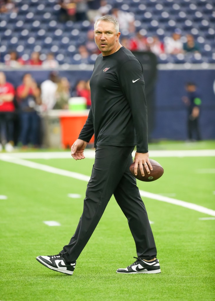 An NFL coach holding a football on the field.