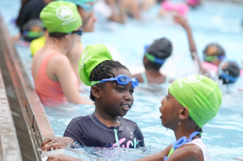 Two children are inside the pool, leaning on the side, chatting.