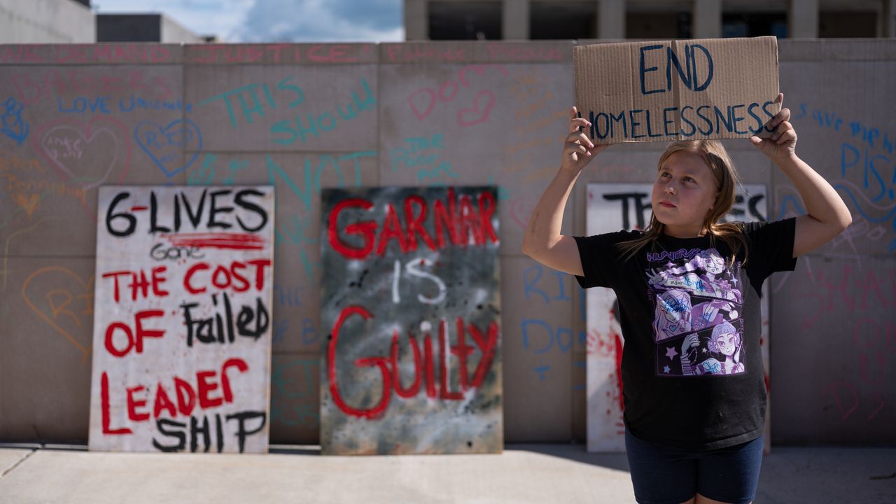 A girl holds a sign that says "end homelessness"