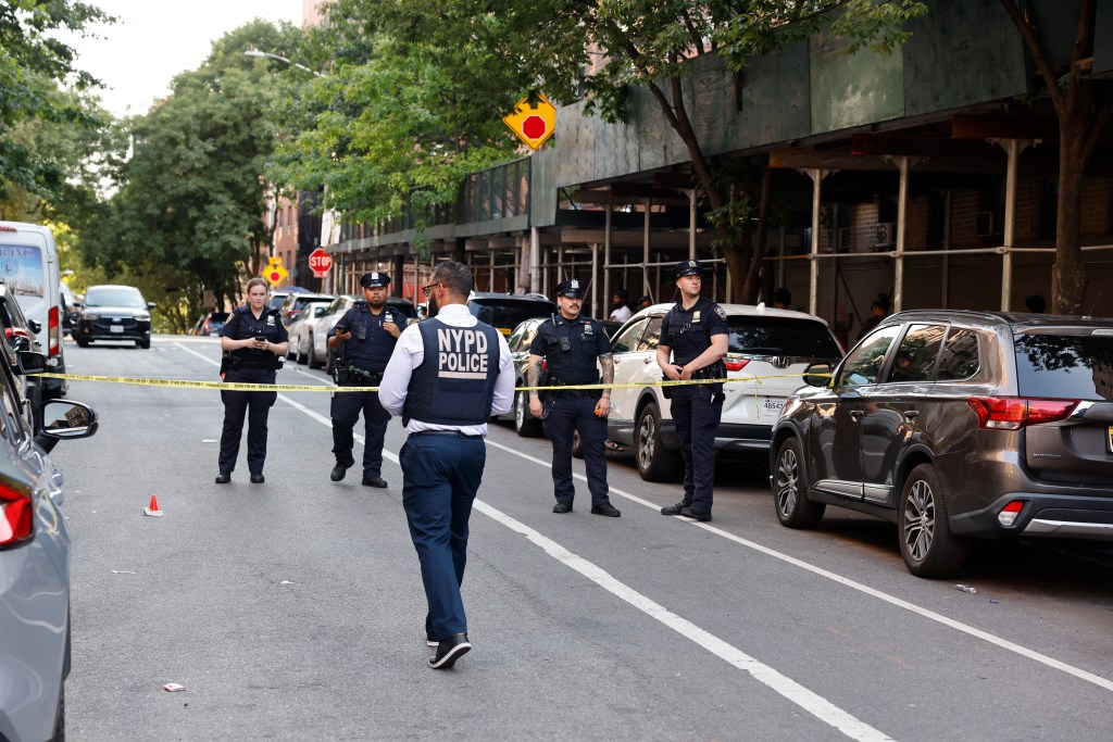 Police investigate a scene with yellow caution tape blocking off a street.