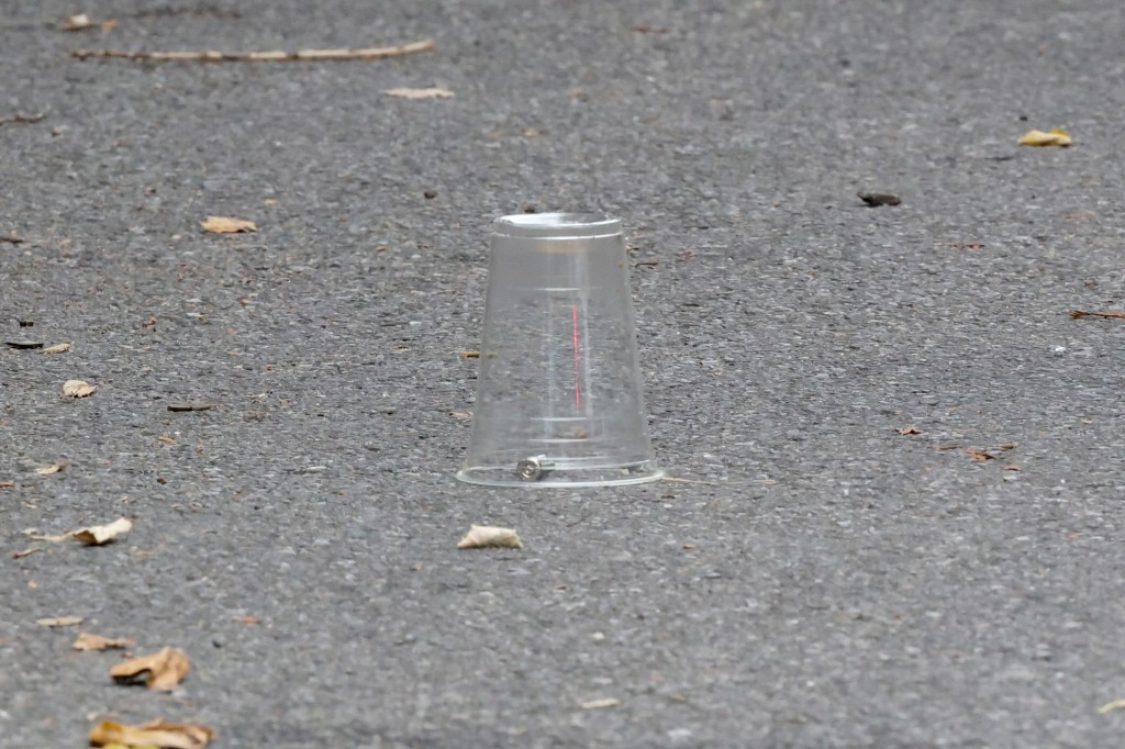 A clear plastic cup on asphalt covers a bullet casing, typical of a crime scene.
