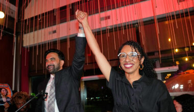 New York City Mayor Zohran Mamdani raising the arm of Darializa Avila Chevalier, who is smiling, at a celebratory event.