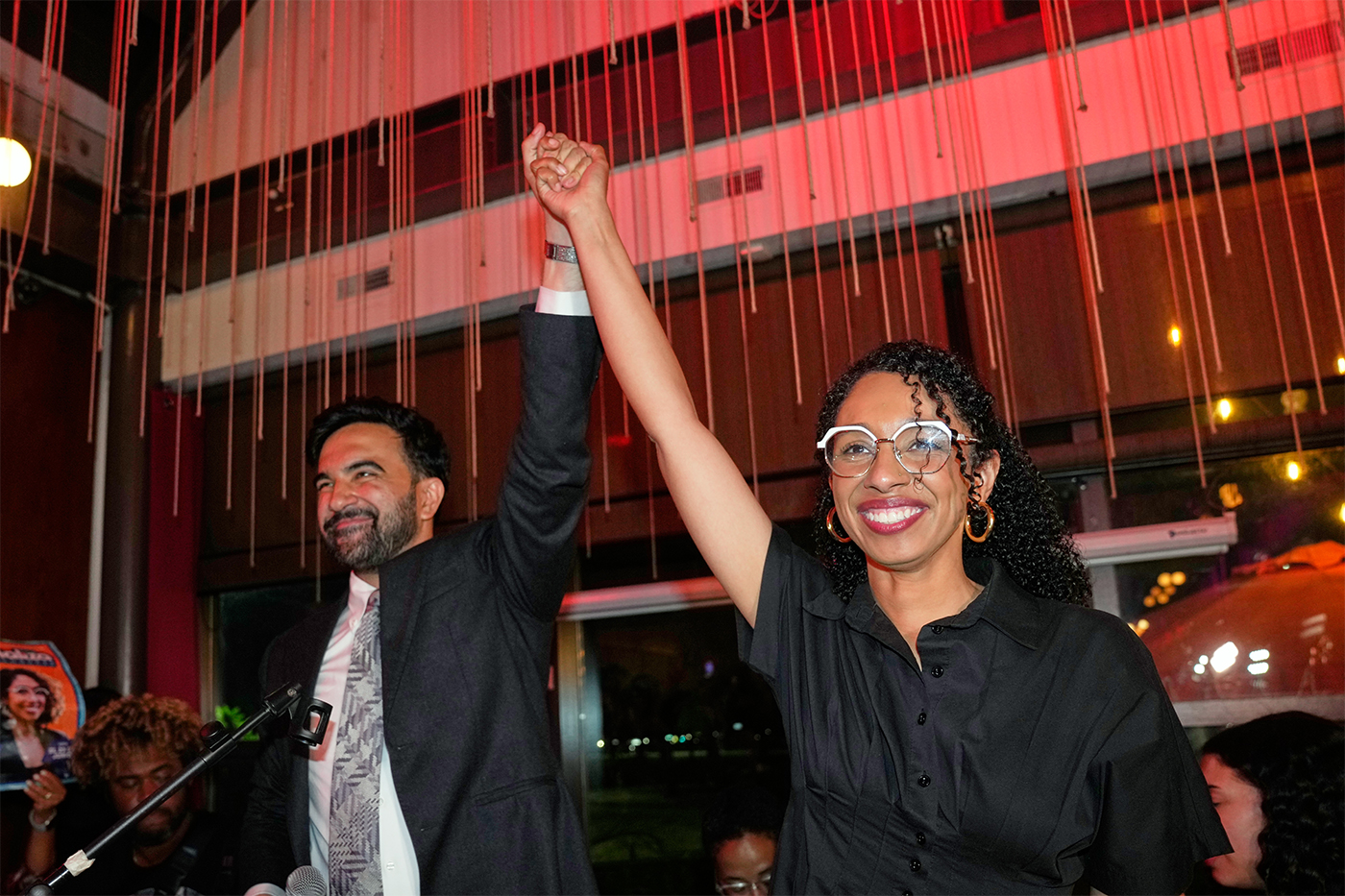 New York City Mayor Zohran Mamdani raising the arm of Darializa Avila Chevalier, who is smiling, at a celebratory event.