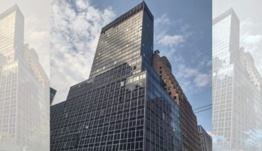 A towering glass and steel skyscraper against a partly cloudy blue sky. The building reflects sunlight, creating a sleek and modern appearance.