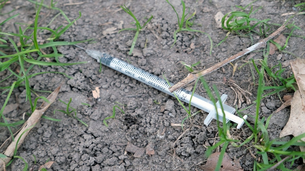 used syringe sits in the dirt at a park