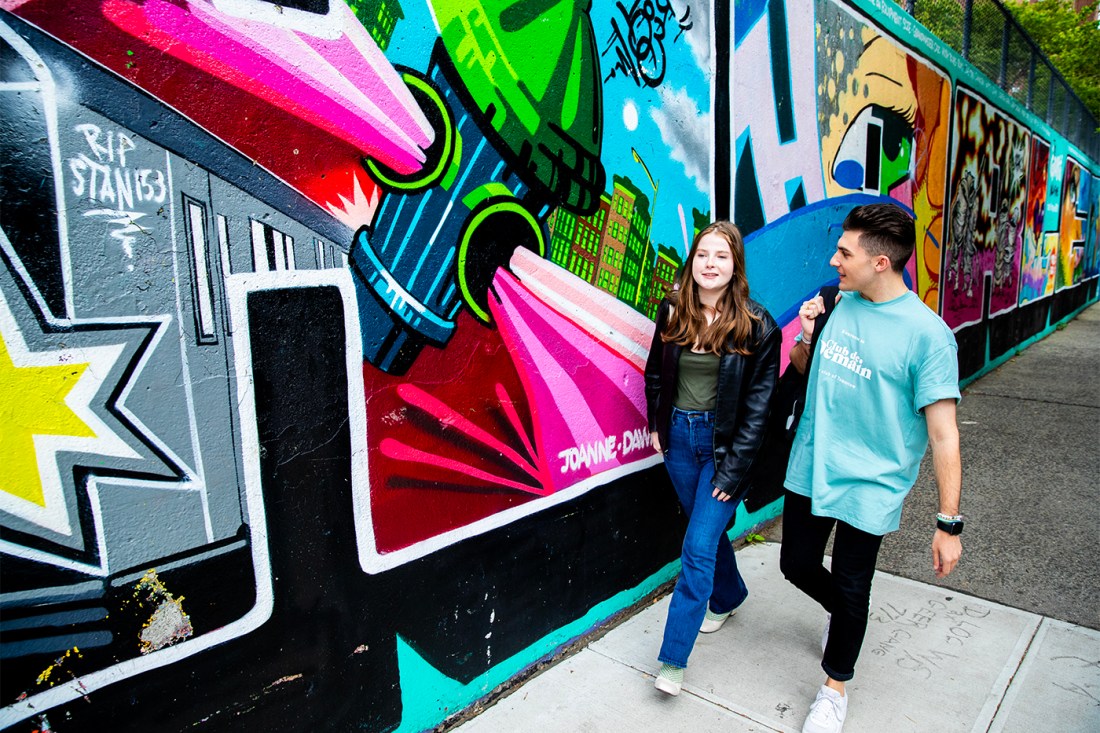 Two students walking along a colorful graffiti mural in New York City.
