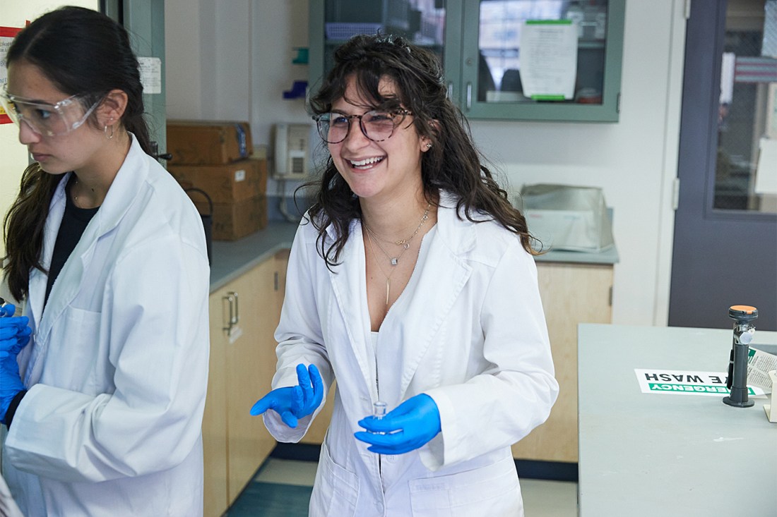 Two students in lab coats and gloves working together in a science laboratory.
