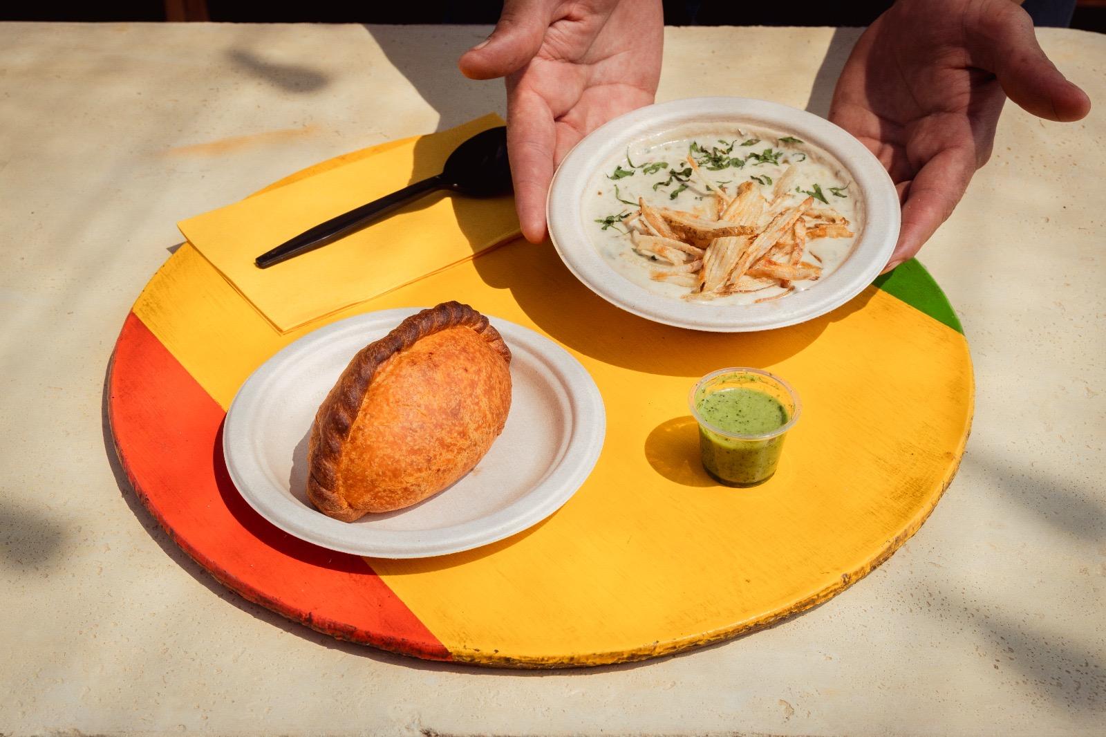 A colorful platter with an empanada and someone putting on a plate of a creamy food.