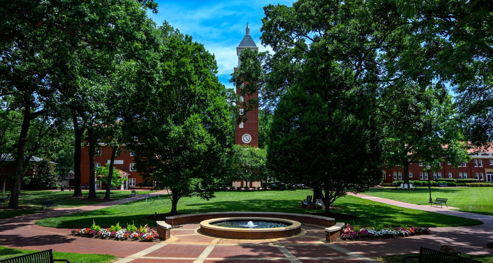 A picture of the Evans Clock Tower on the Queens University campus with a brick plaza in the foreground and trees surrounding the view.
