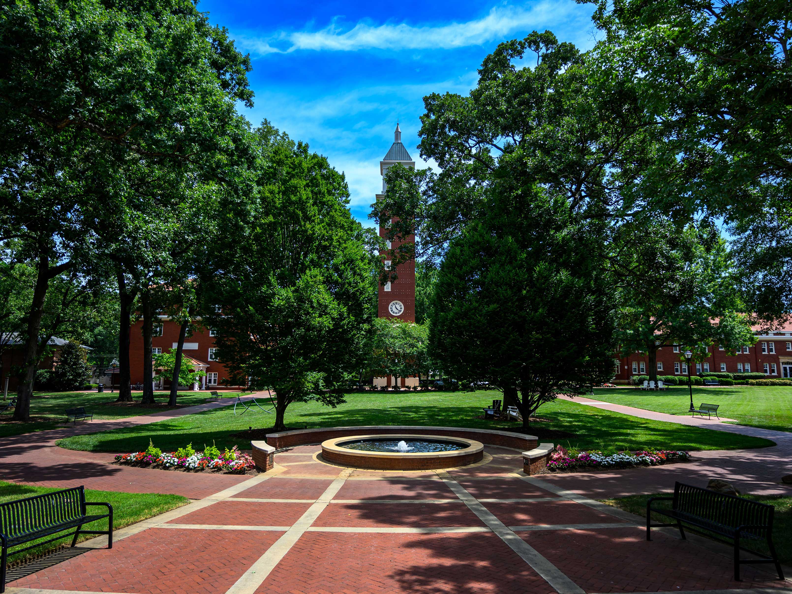 A picture of the Evans Clock Tower on the Queens University campus with a brick plaza in the foreground and trees surrounding the view.