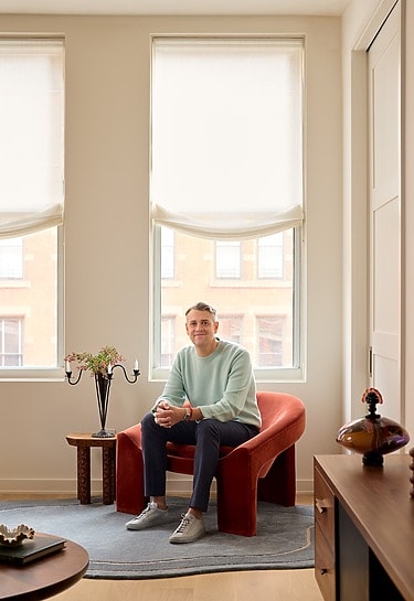 Person sitting in a red chair near bright windows in a modern living room setting.
