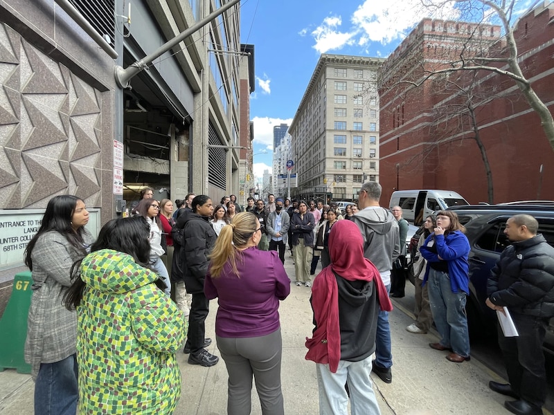 An individual standing on a sidewalk speaking to a crowd.