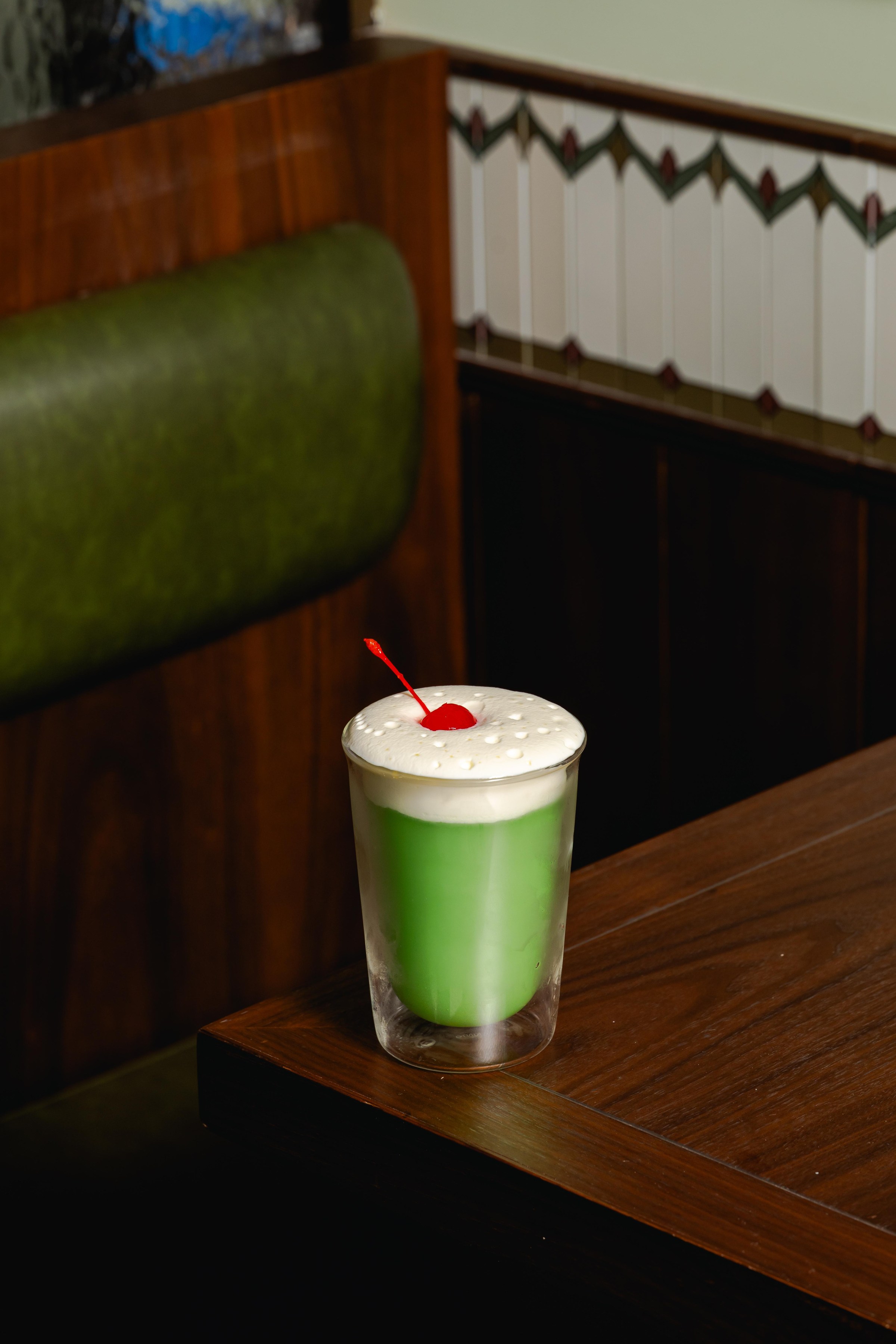 A green cocktail with a frothy cream top and a cherry.