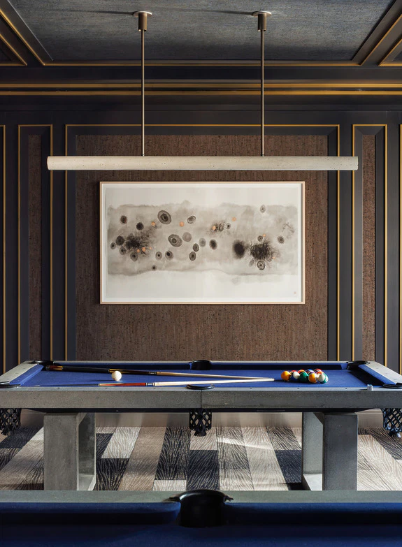 Modern game room with a blue pool table, billiard balls, wall art, and sleek lighting fixture.
