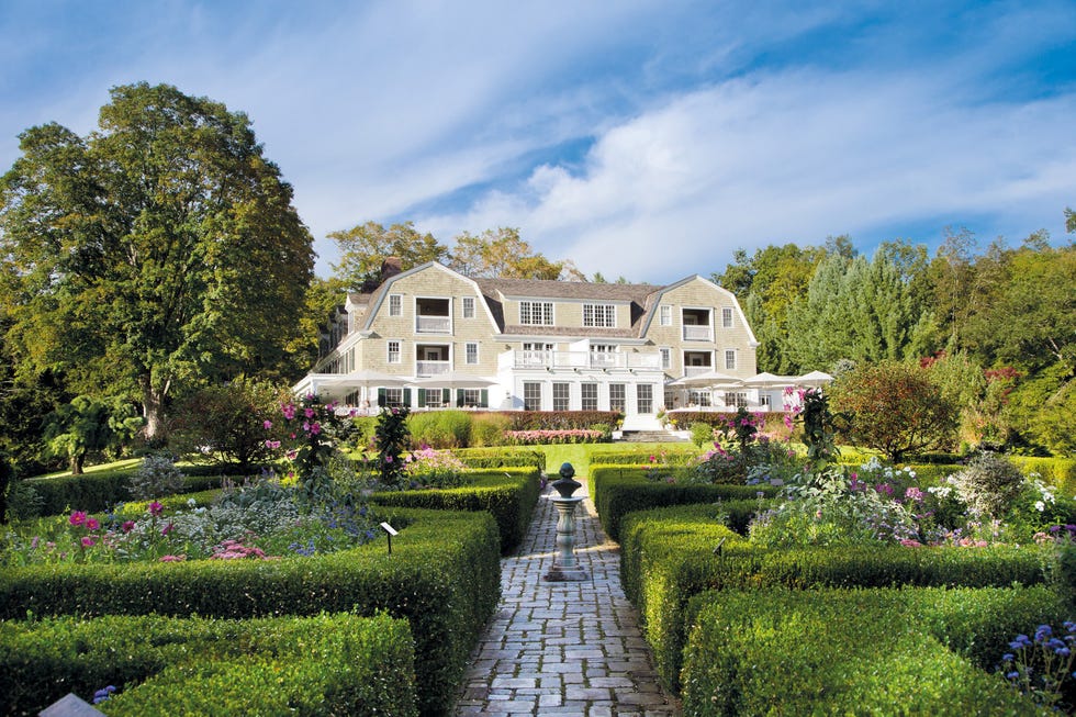 Elegant garden with manicured hedges and colorful flowers in front of a large, picturesque house under a blue sky. Elegant garden with manicured hedges and colorful flowers in front of a large, picturesque house under a blue sky.