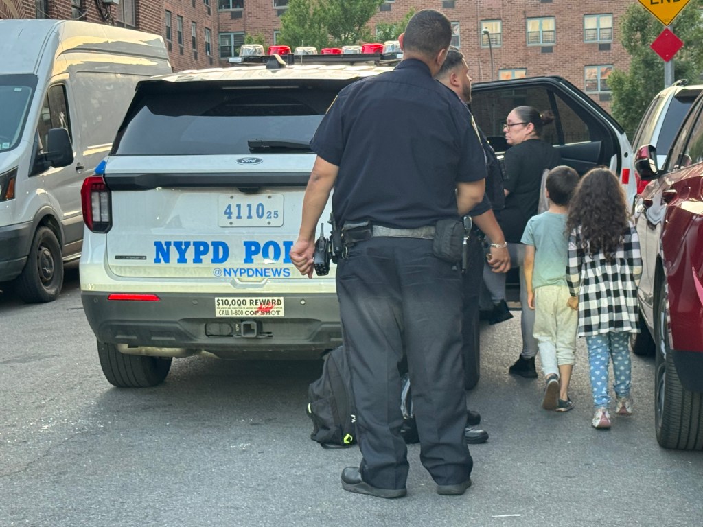 Police escorting a man in handcuffs and children at the scene of a child falling from a window.