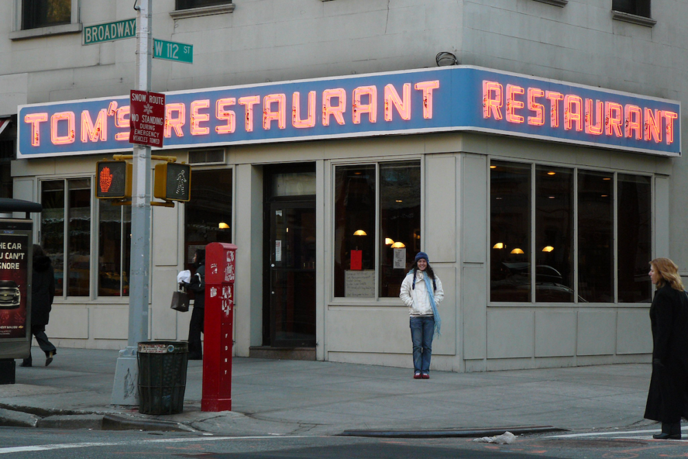 Image: a woman stands in front of Tom's Restaurant in New York City, famous to viewers of Seinfeld.