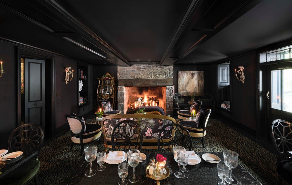 Cozy interior with a stone fireplace and elegant seating, dimly lit with candles and a table set for dining. Cozy interior with a stone fireplace and elegant seating, dimly lit with candles and a table set for dining.
