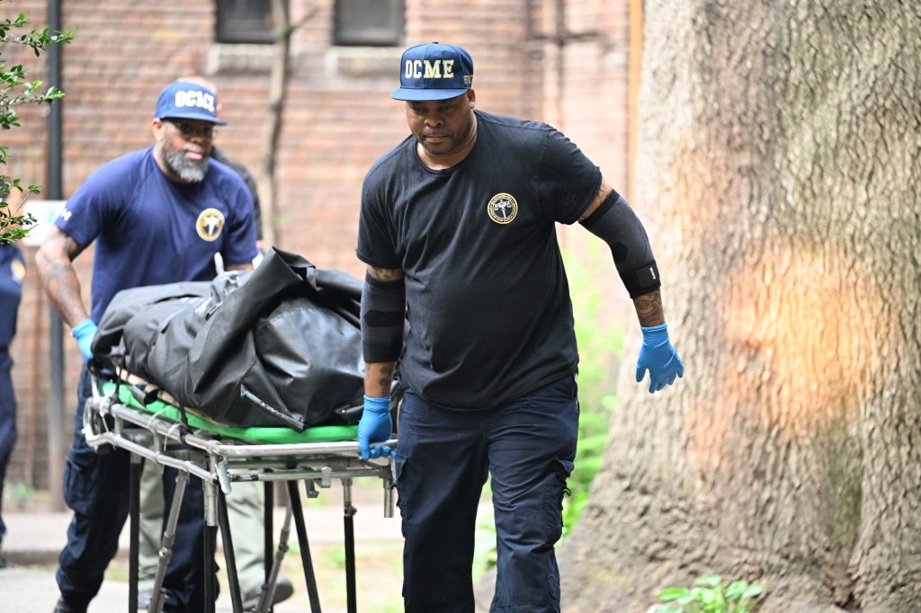 Two men in uniform removing a body in a black bag on a stretcher from an apartment building.