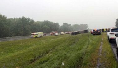 emergency crews at scene of bus rollover in median strip of highway on a cloudy morning