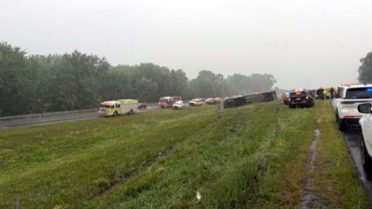 emergency crews at scene of bus rollover in median strip of highway on a cloudy morning
