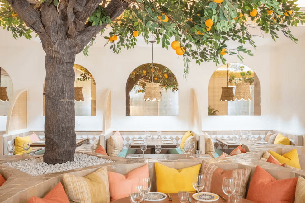 Chic restaurant interior with tree centerpiece, vibrant pillows, and hanging woven lamps.