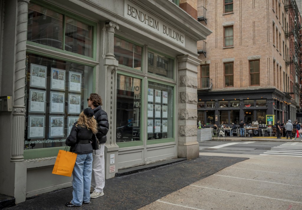 A couple view properties for sale in the window of an estate agent's office in New York City.
