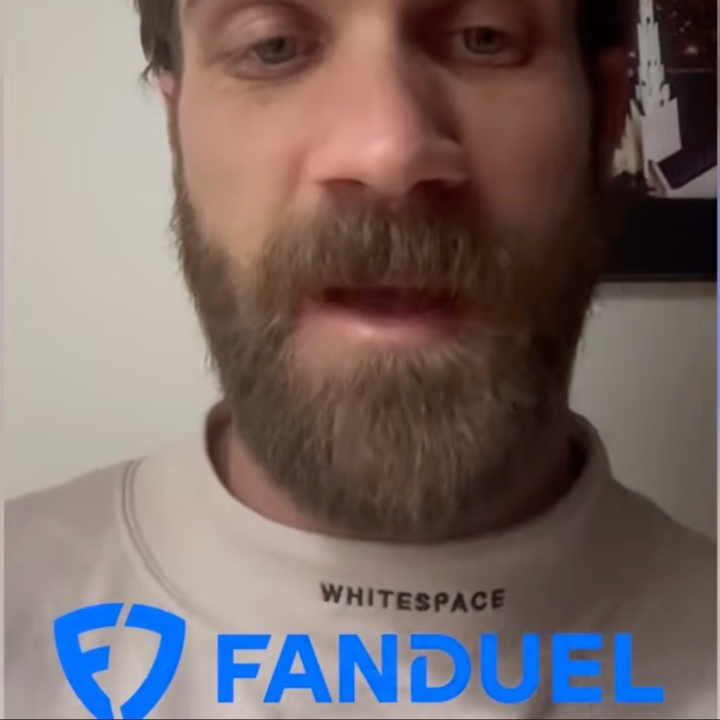 Bryce Harper with a beard wearing a white sweatshirt and a FanDuel logo.