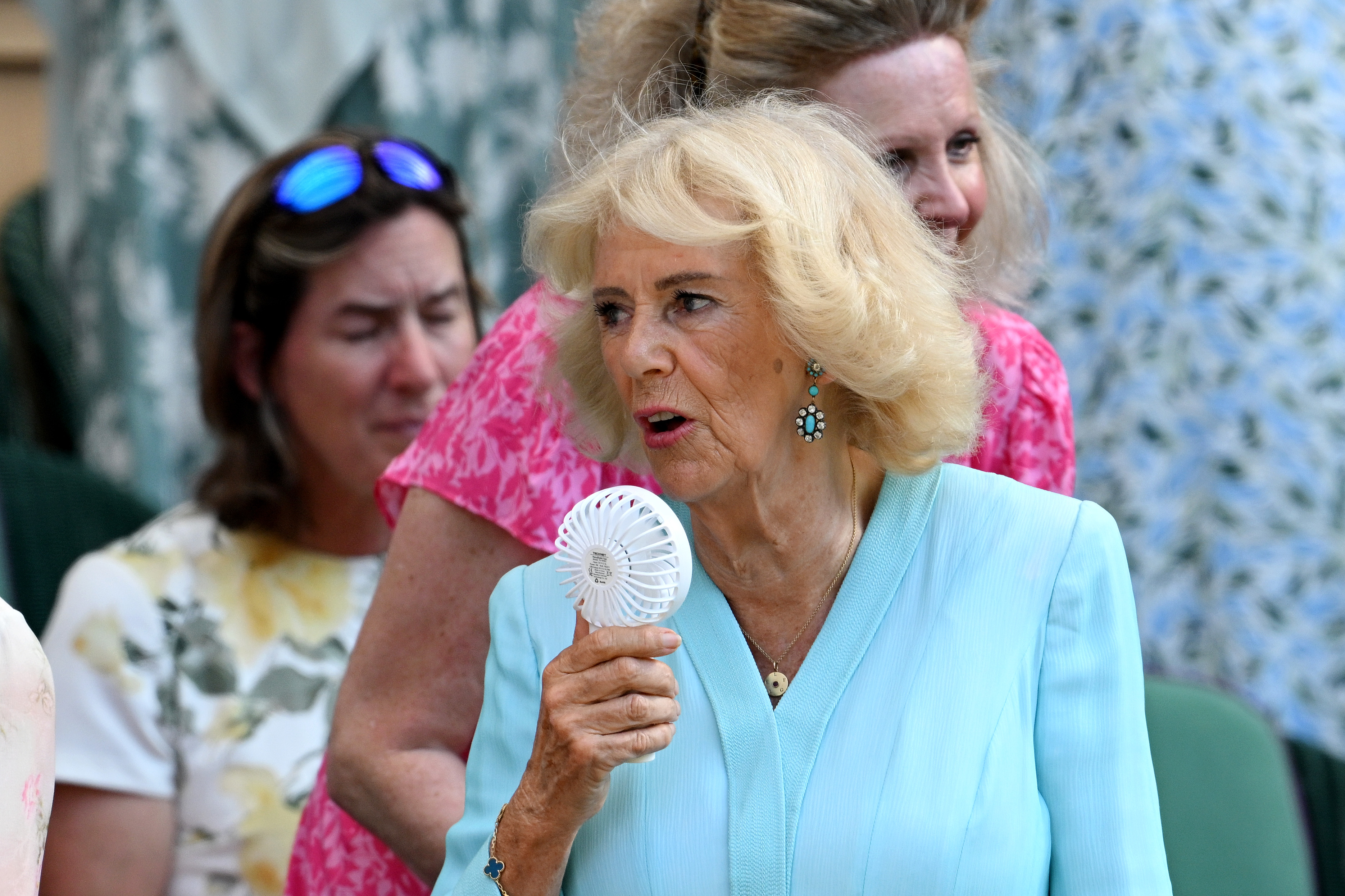Queen Camilla wearing a blue dress and holding a fan