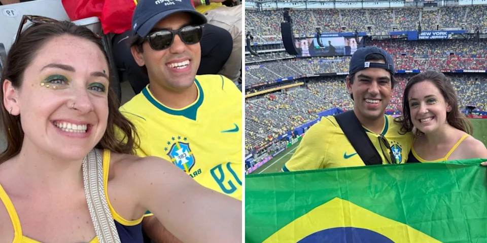 Two smiling Brazil soccer supporters pose with a Brazil flag inside a crowded stadium.