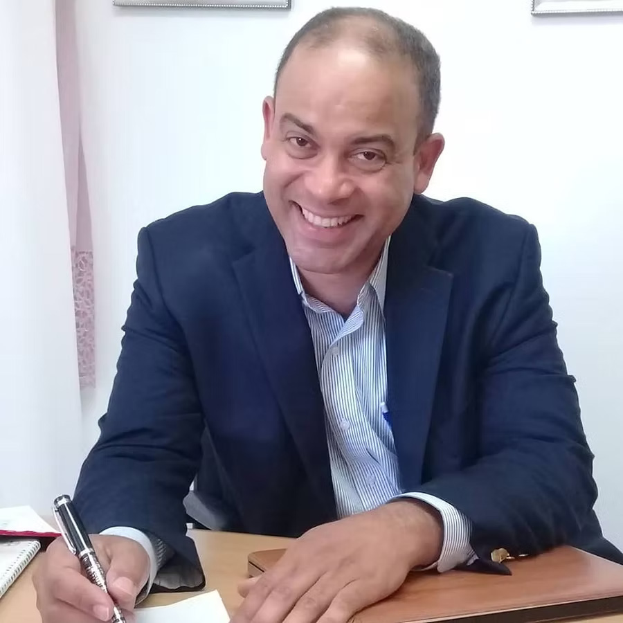 Dr. Luis A. Rojas, esthetician at Bereshit Lifestyle Center, smiling while writing at his desk.