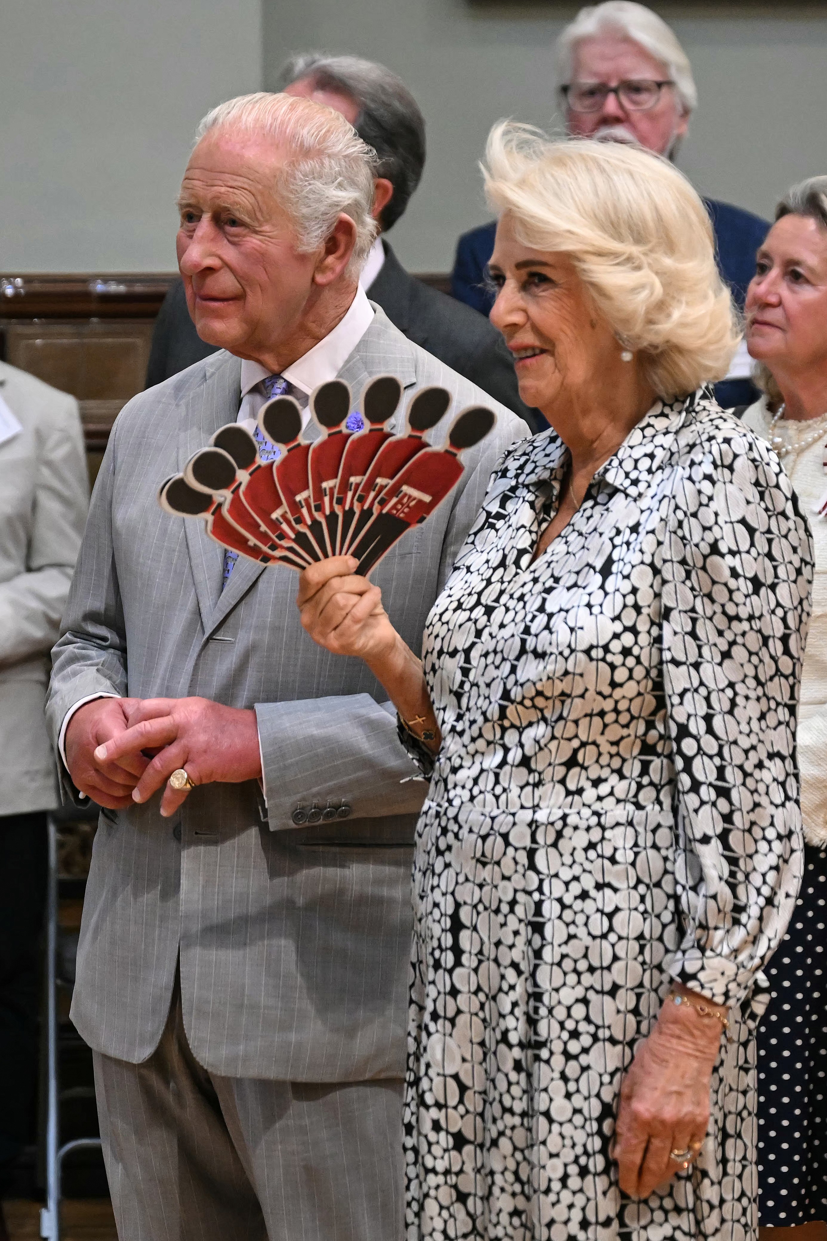 Queen Camilla waving a British soldier fan standing next to King Charles