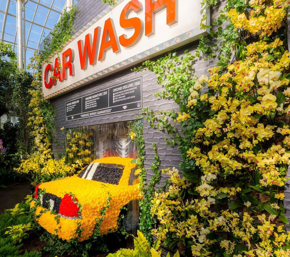 Floral car wash display with a yellow car covered in vibrant flowers and greenery ay NYBG
